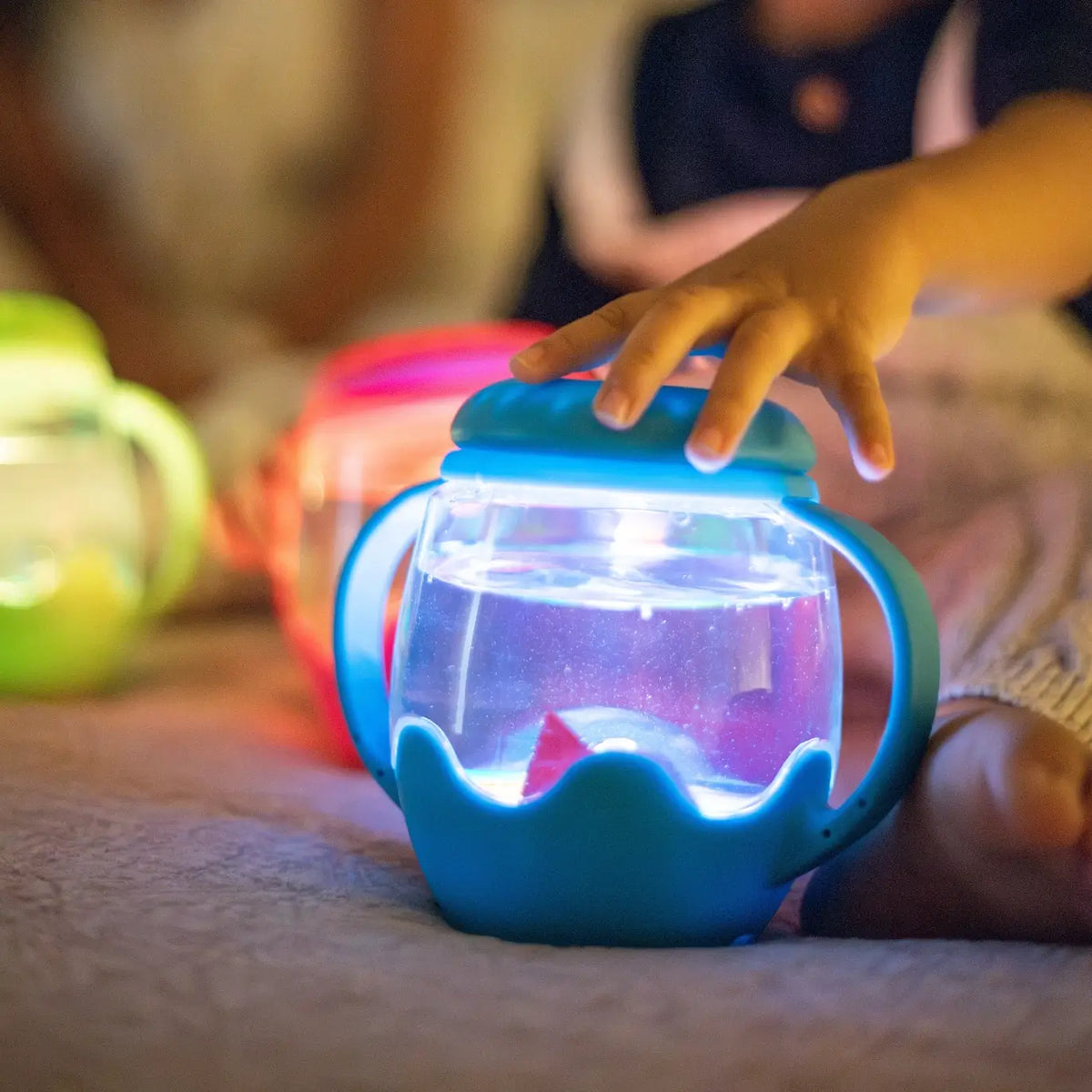 A toddlers hand touches the top of the Blue Glo Pals Mini Sensory Jar and Silicone Fun Filler.