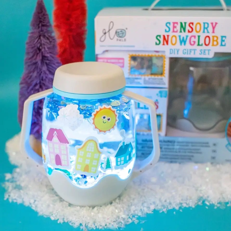 A glowing sensory jar covered in stickers sits in front of the product package for the Glo Pals Sensory Snowglobe DIY Gift Set.