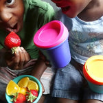 Two children eat strawberries while holding two different GoSili 8 oz Silicone Kids to Go Travel Cups.