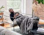 A man reclines on a soft chair with the Grey Gravity Weighted Blanket draped over his lap.