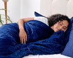A woman rests in a bed on her side while wrapped in the Navy Gravity Weighted Blanket.