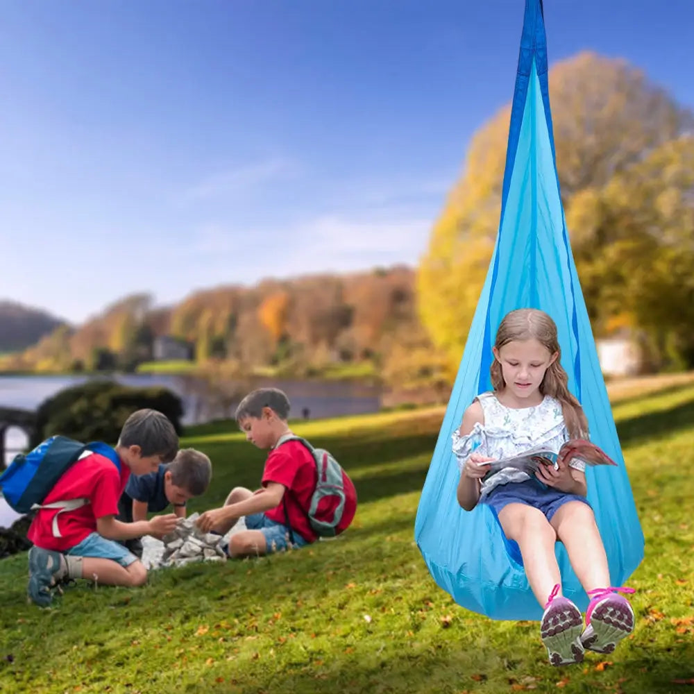 A child hangs from the Sensory Pod Swing and reads in an outdoor setting.