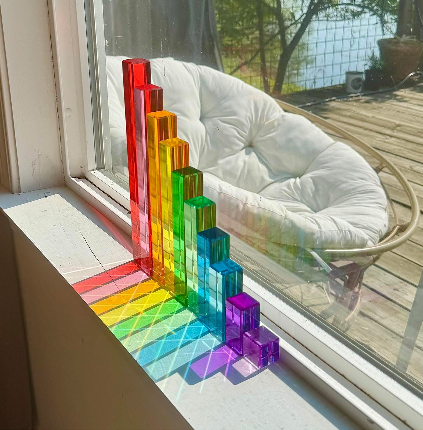The 10-Piece Crystal Clear Pyramid Lucite Blocks arranged tallest to smallest, reflecting colorful light from the window.