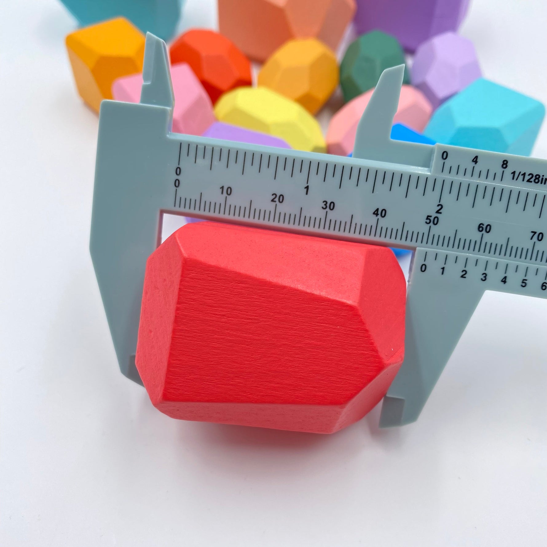A pastel red Wooden Balancing Stones Stacking Block being measured by a blue tool.
