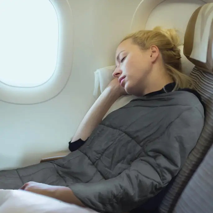 A person sleeping on an airplane is draped in the Grey Microfiber Weighted Throw Blanket 5 lbs.