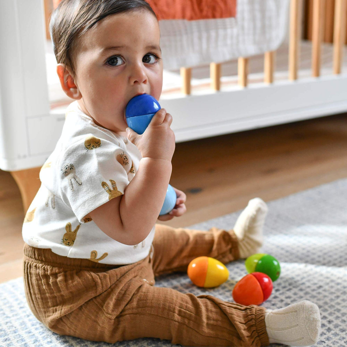A toddler puts the blue Fun With Sounds Wooden Egg into his mouth.