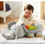 A baby sits up and explores the Baby Elephant Discovery Sensory Pillow.