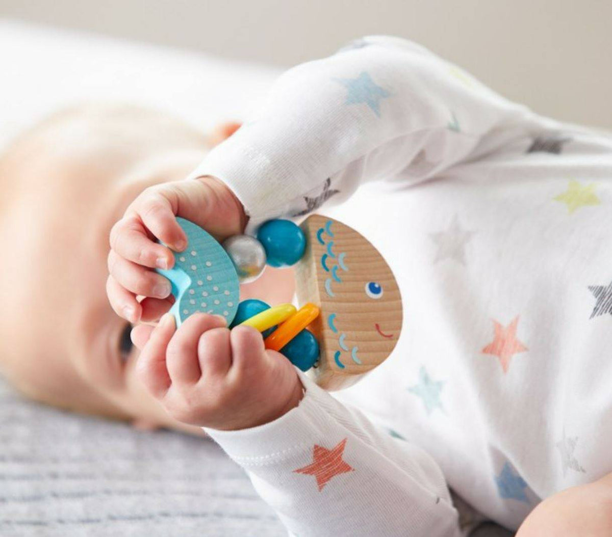 A baby holds up the Rattlefish Baby Wooden Rattle.