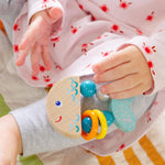 The Rattlefish Baby Wooden Rattle sits on a baby's leg.