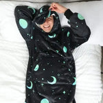 Someone wears the Hideout Hoodie Galactic Glow Wearable Blanket Hoodie in a bed with the built-in mask pulled down.
