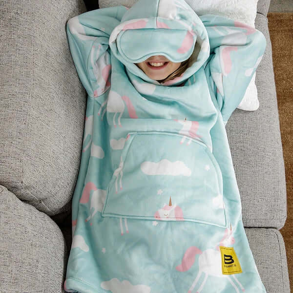 A child lays on a couch with their arms behind their head, cozy in their Unicorn Kids Hideout Hoodie.