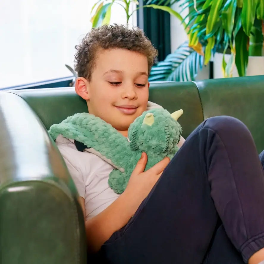 A child sits on a leather sofa while holding Zephyr the Dragon on their chest.