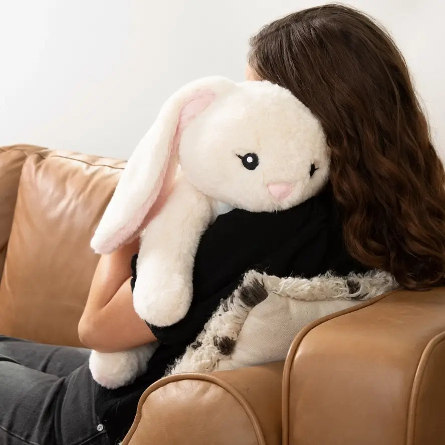 Someone sits on a leather couch while holding Iggy the Bunny over their left shoulder.