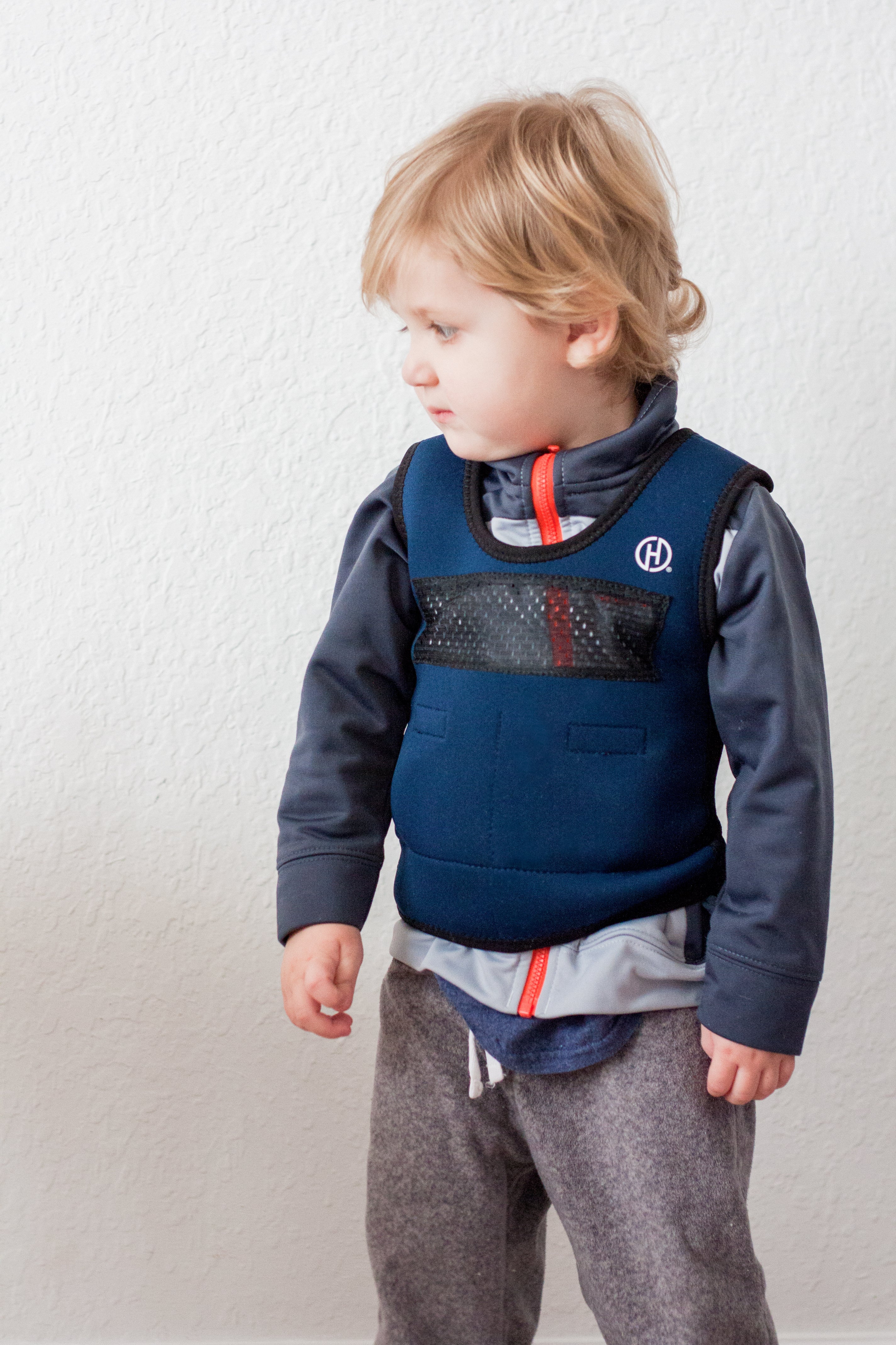 A child with light skin tone and short blonde hair is wearing a Weighted Compression Vest over their sweat shirt.