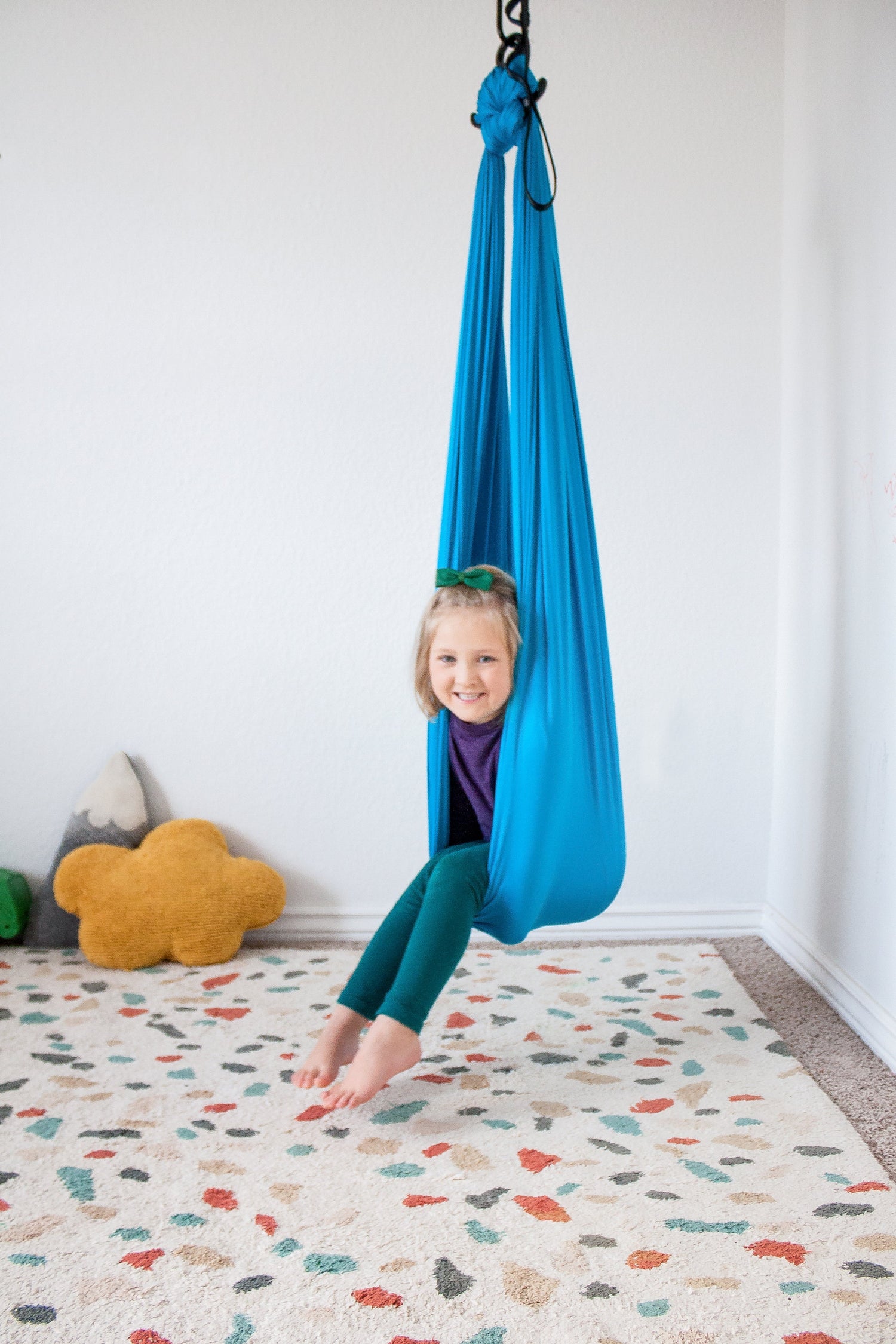 A child with light skin tone looks out of a blue compression swing they are sitting in. 