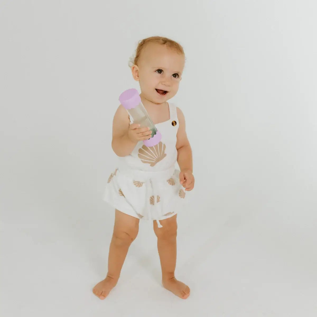 A toddler stands while holding the Bubblegum Baby Calm Down Bottle.