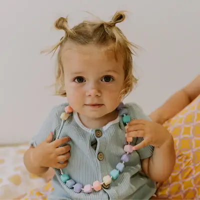 A 3-year-old with space buns wears the pastel Princess and the Pea Necklace.