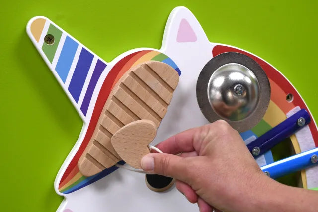 A hand with light skin tone plays on the wooden percussive instrument on the Unicorn Activity Wall Panels.