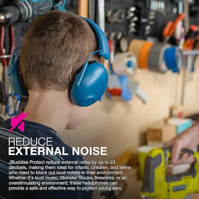 A child stands in a home shop wearing their The Jlab Navy Jbuddies Protect Kids Hearing Protection Earmuffs while an adult uses a power saw.