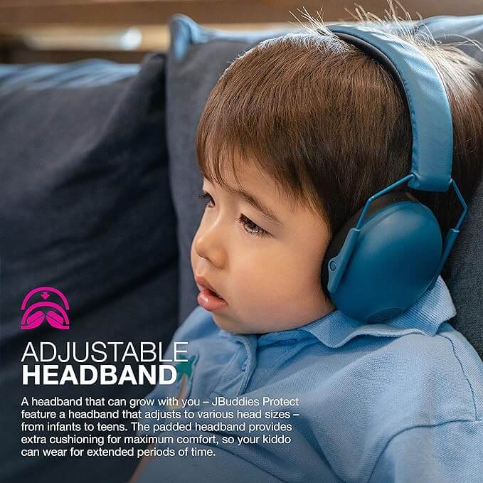 A toddler sits on a couch wearing a pair of the Jlab Navy Jbuddies Protect Kids Hearing Protection Earmuffs.