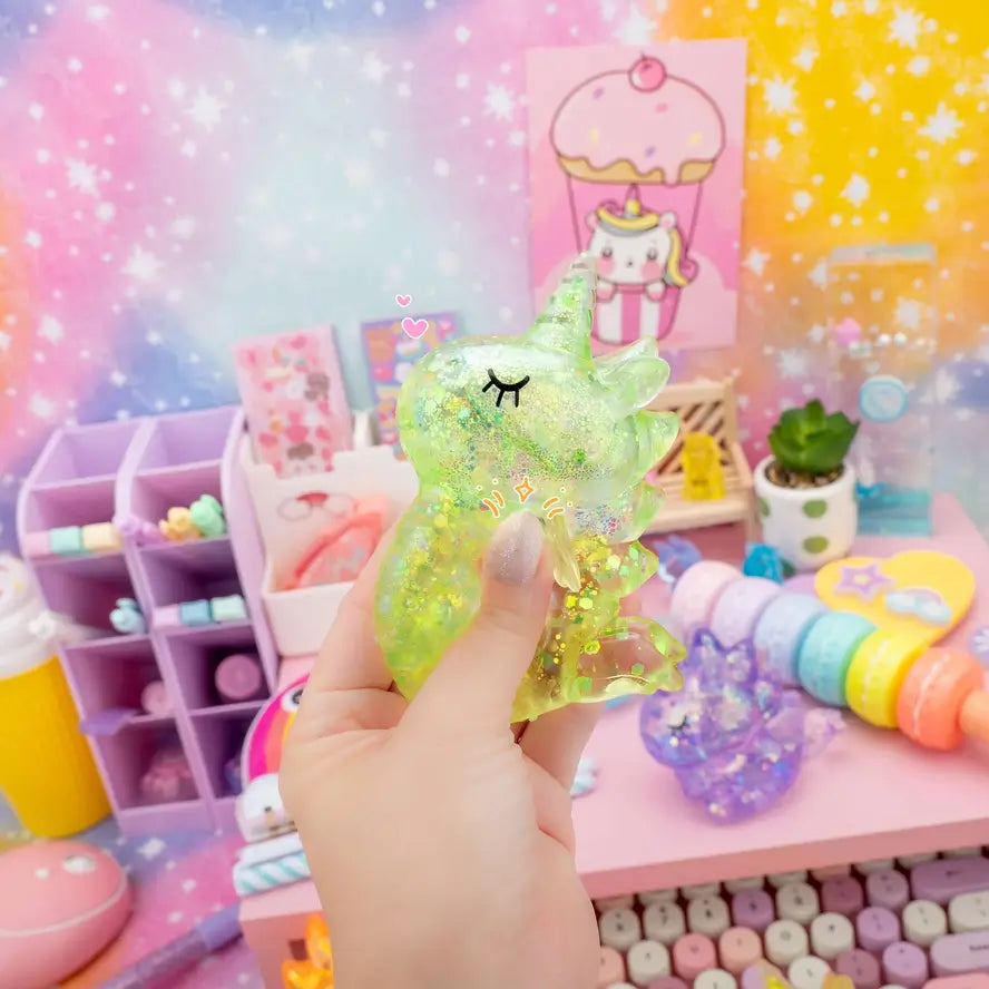 A hand holds up a green Gummy Unicorn Friend in front of a colorful backdrop.