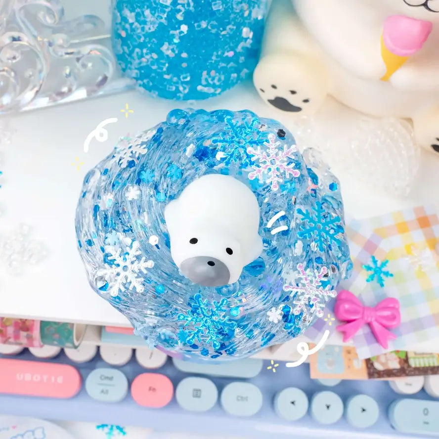 The squishy polar bear that comes in the Polar Bear Plunge Clear Slime sits on top of a mountain of clear slime full of snowflakes of varying sizes.