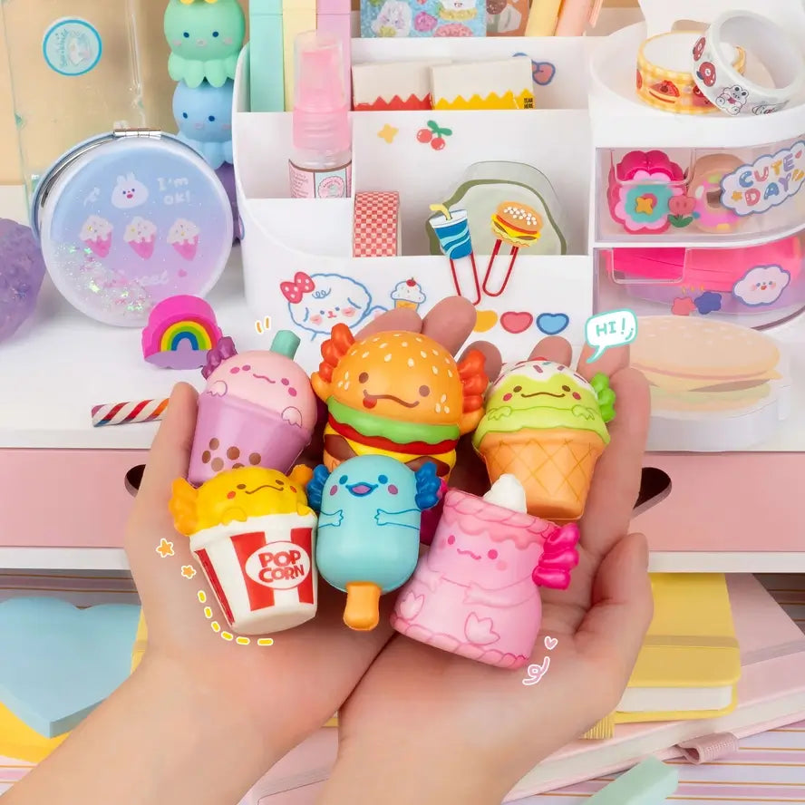 Two hands hold up a variety of the Snaxolotls in front of a colorful Kawaii display.