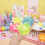 A hand holds an assortment of the Gummy Kitty Paw Squishes in a colorful scene with office supplies.