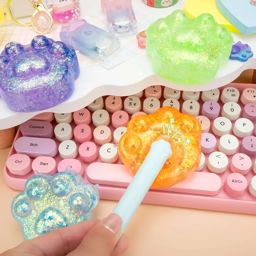 A hand high-fives the orange Gummy Kitty Paw Squish with a tiny toy cat paw.