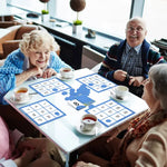Four seniors sit around a recreation table with cups of tea; they are laughing and playing a game of Easy Bingo.