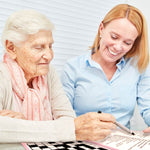 A senior sits with another person while looking over the key for Keeping Busy's Season Easy Crossword Puzzle.