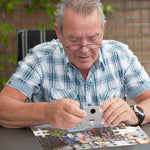 A senior holds up a large puzzle piece with a black dot on the underside.