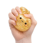 A hand squeezing the golden glittery  Lucky Bao Mystery Squishy Dumpling.