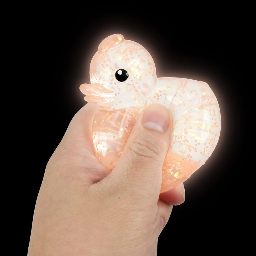 A hand holds a glowing orange glitter Stretchy Glow Duck.