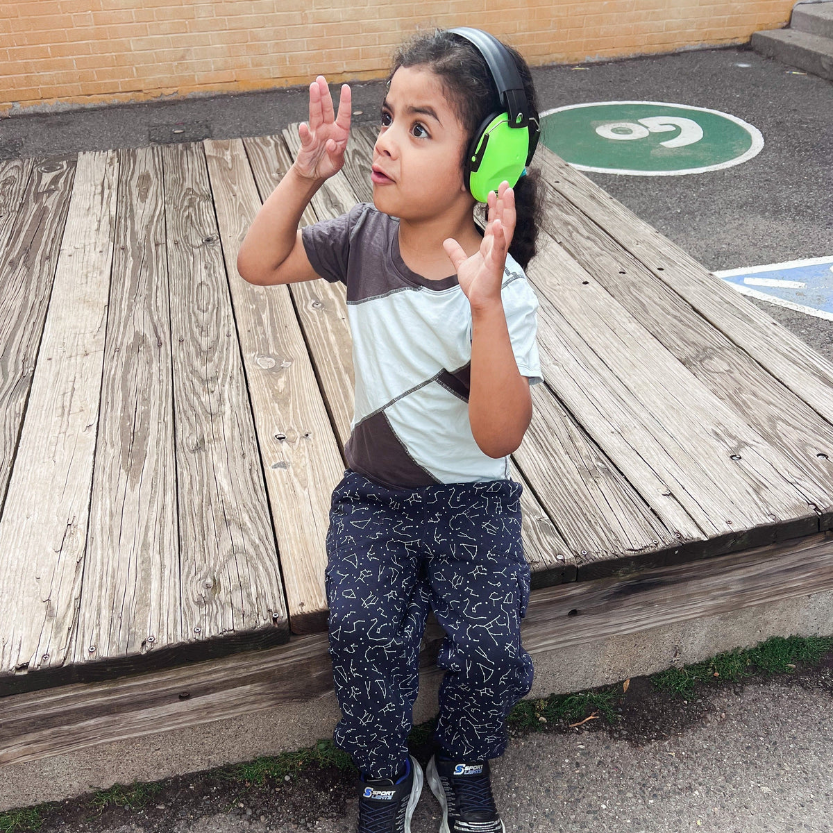 A child with noise reducing earmuffs also wears the Grey-Mint Kids Compression Lined Sensory T-shirt.