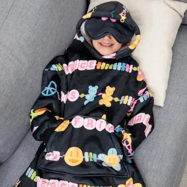 A child models the Kids Friends Forever Hideout Hoodie while laying on a couch, their hands in the kangaroo pocket and the built-in eye mask down.