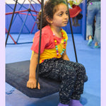 A child sits on a carpeted sensory swing wearing the Contellation Print Kids Sensory Friendly Fidget Jogger.