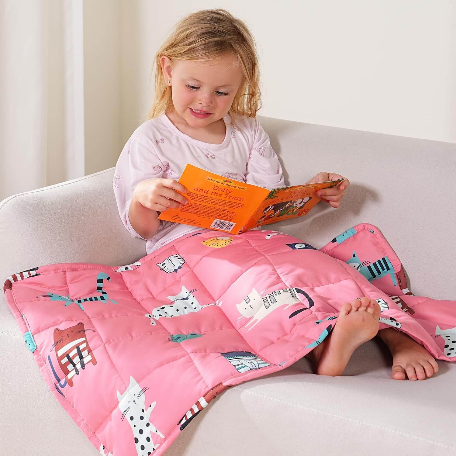 A child reads a book while perched on a couch under thee Kitties Weighted Cooling Lap Pad 2 lb.