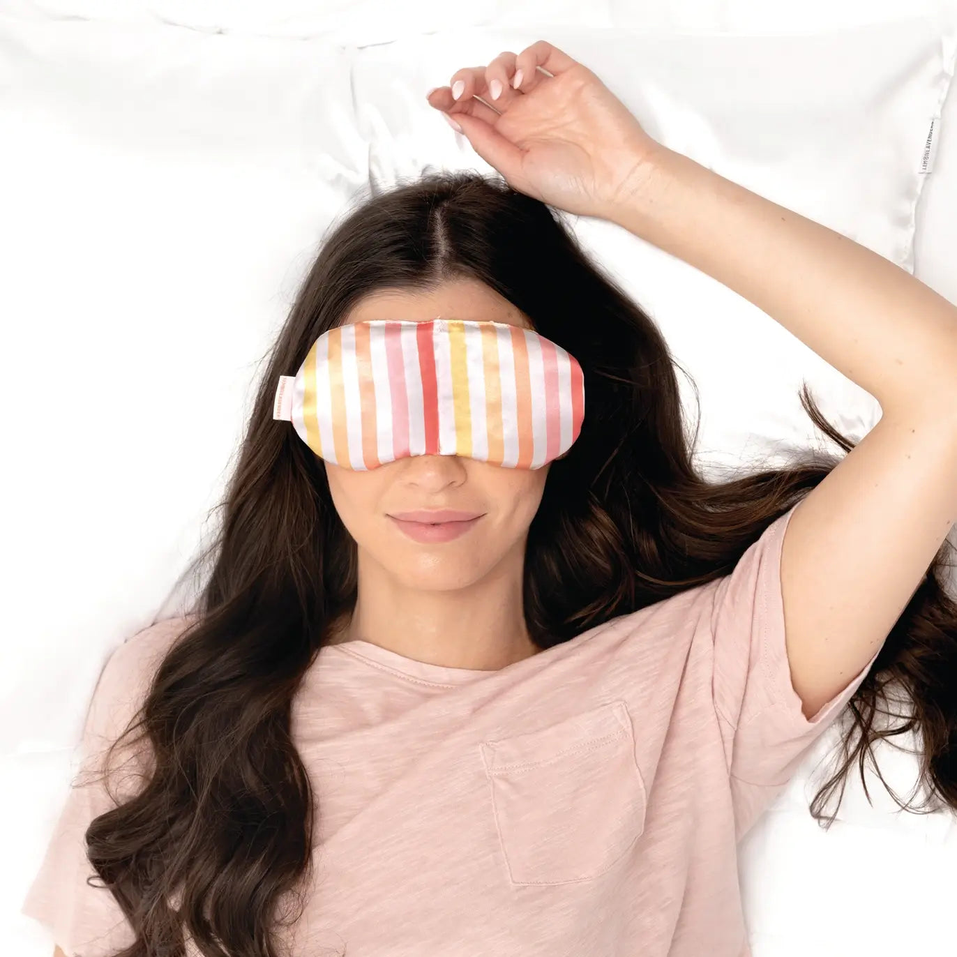 A woman smiles and relaxes on a bed while wearing the Cabana Stripe Under Pressure Weighted Eye Mask.