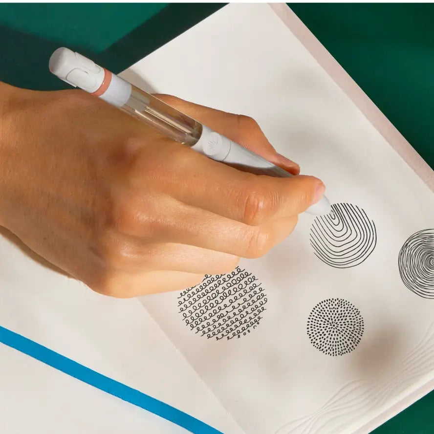 A hand doodles using the Lifelines Spiced Chai Latte Essential Oil Pen Diffuser  on an embossed page.