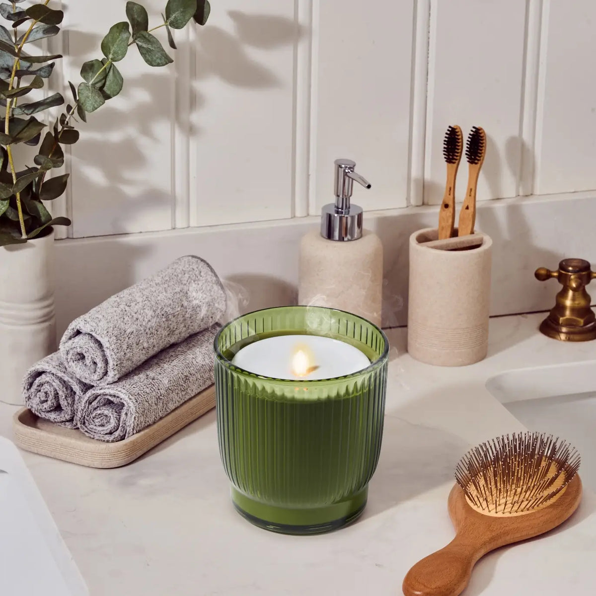 The Olive Flameless Candle Diffuser emits a soft glow next to a bathroom sink.