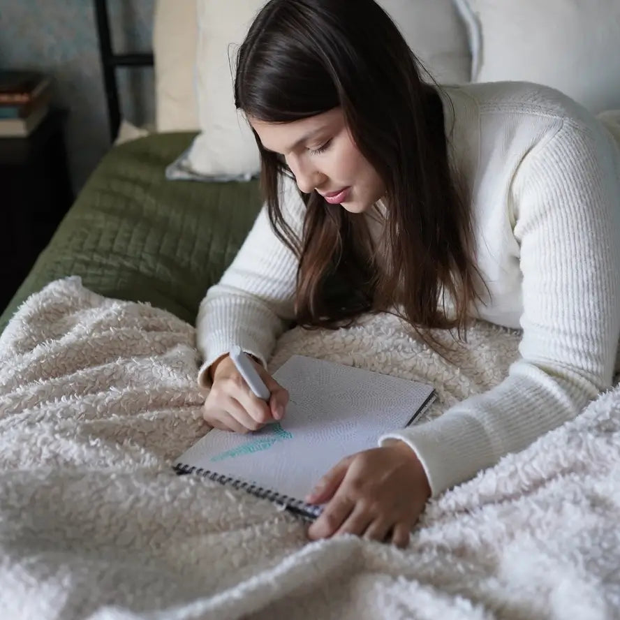 A woman lays in bed while filling in the Lifelines FlowArt Dot-by-Letter Pad.