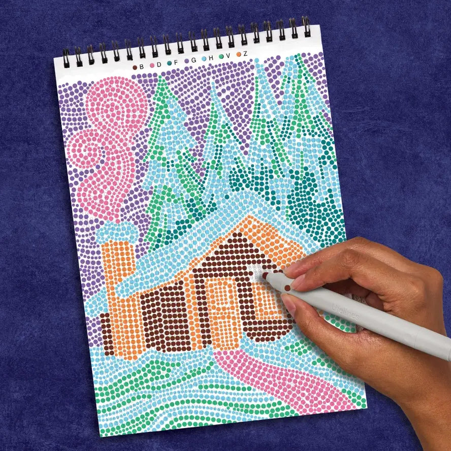 A hand fills in the color matching the letters on this FlowArt scene of a cabin covered in snow in the woods.