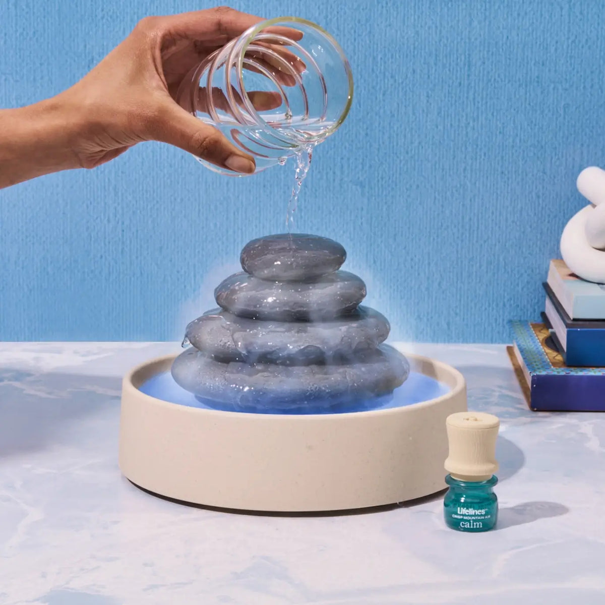 A hand pours water out of a glass and onto the Lifelines Stacking Stone Diffuser.