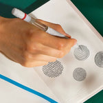 A hand holds the Pen Diffuser and doodles on an embossed piece of paper.