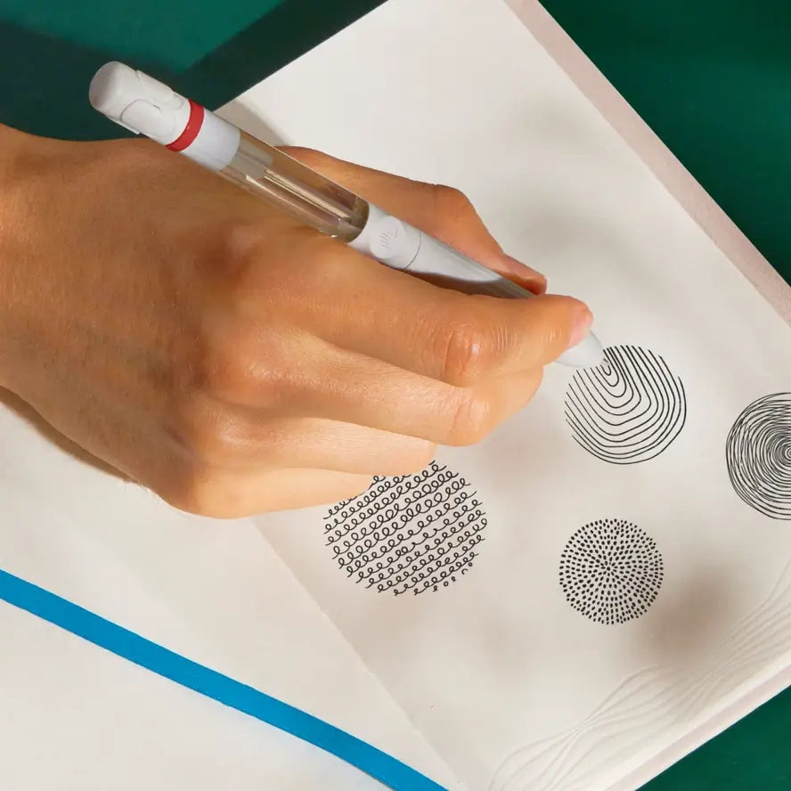 A hand holds the Pen Diffuser and doodles on an embossed piece of paper.