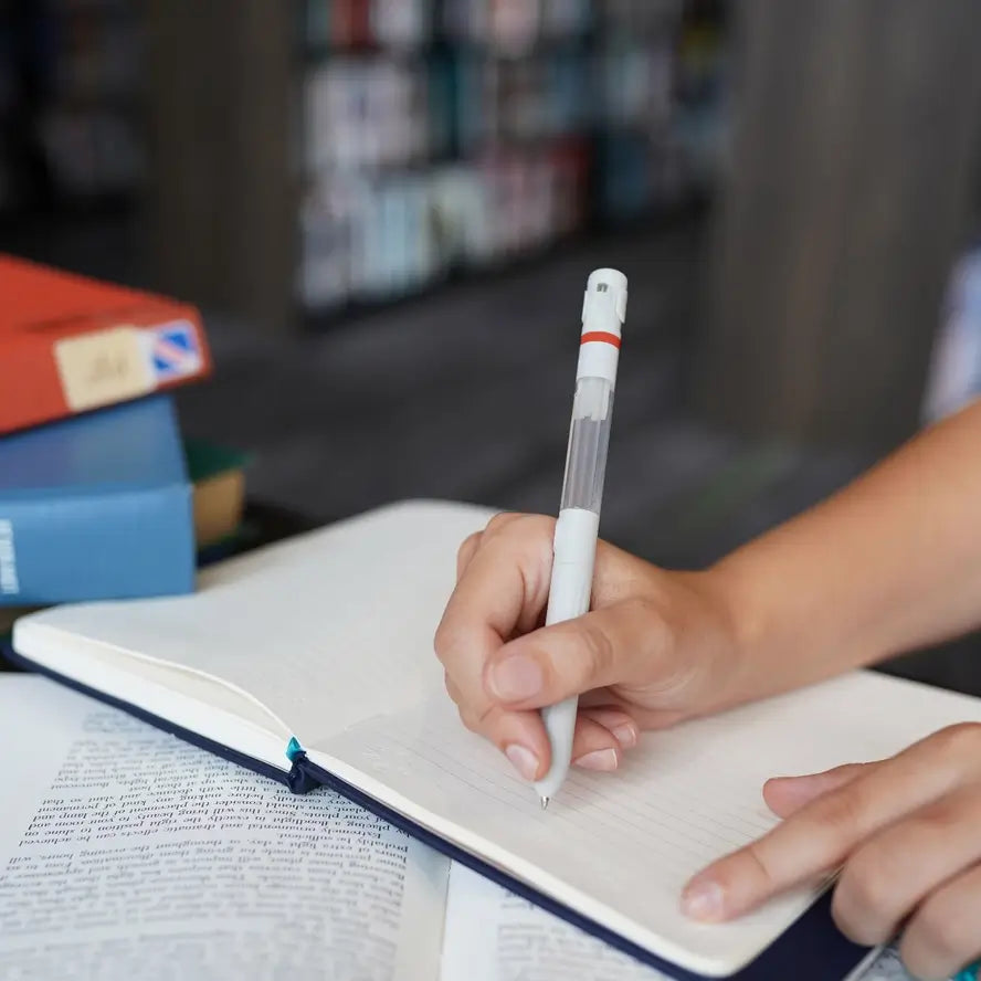 A pair of hands hold open a journal, and one is poised above a page with the Lifelines Pen Diffuser.