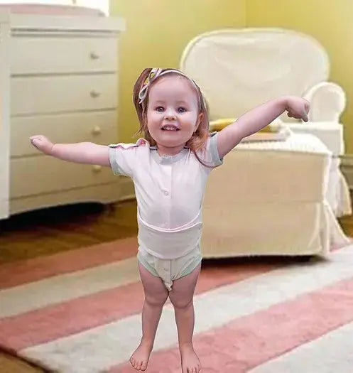 A child wears the Light Pink Kozie Medical and G-Tube One-Piece Bodysuit - The Susie.