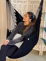 A woman relaxes in the Black Boho Hammock Chair Swing.