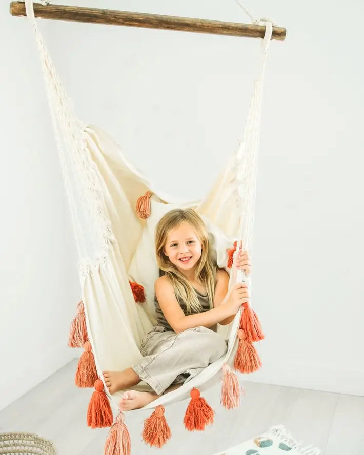 A child curls up in the Junior Hammock Chair Swing with Pink Tassels.